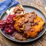 Jägerschnitzel with mashed potatoes and red cabbage on grey plate.