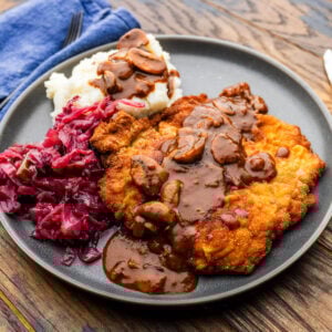 Jägerschnitzel with mashed potatoes and red cabbage on grey plate.