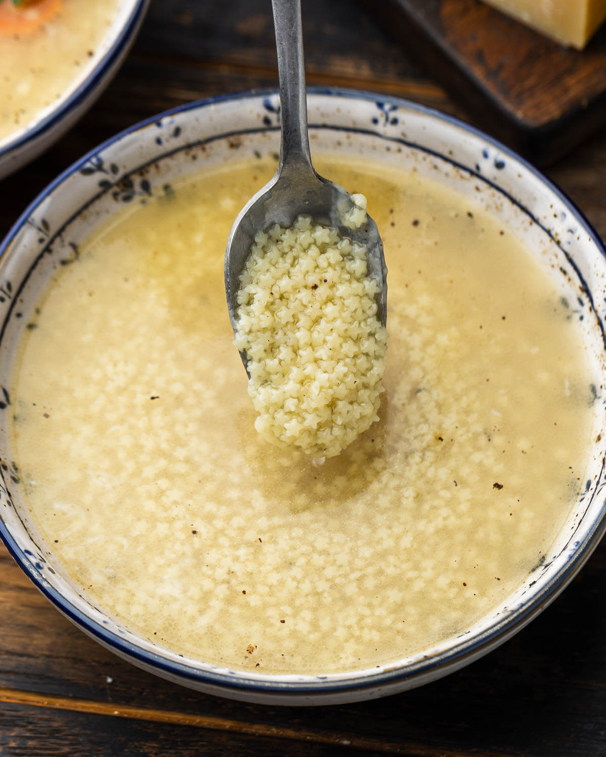 Spoon holding pastina over bowl.