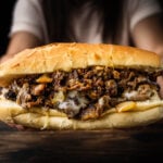Hands holding Philly cheesesteak over table.