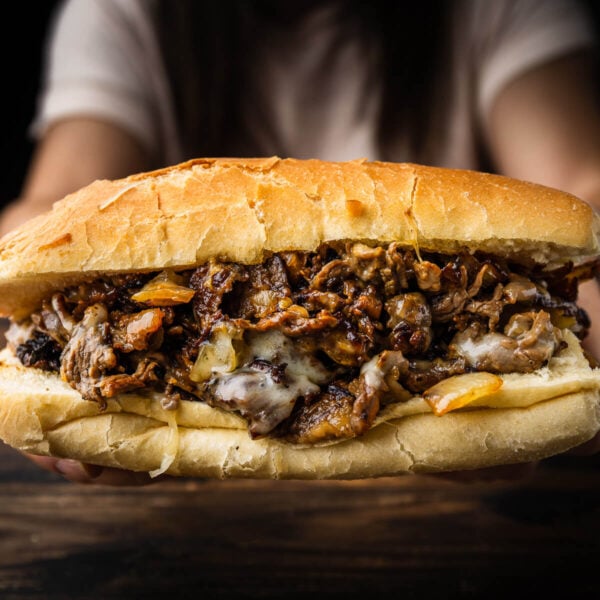 Hands holding Philly cheesesteak over table.