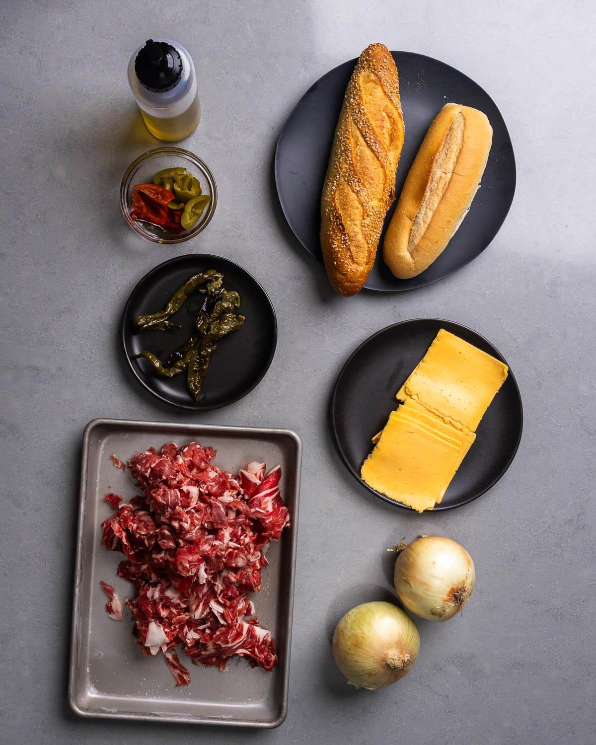 Ingredients shown: oil, cherry peppers, Italian long hots, hoagie rolls, sliced ribeye steak, American cheese, and onions.