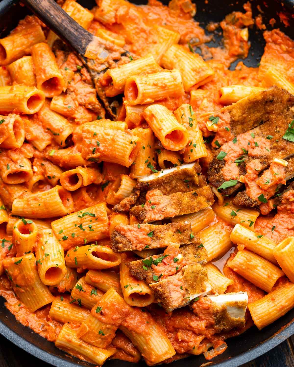 Large pan with spicy vodka rigatoni and sliced chicken cutlets.
