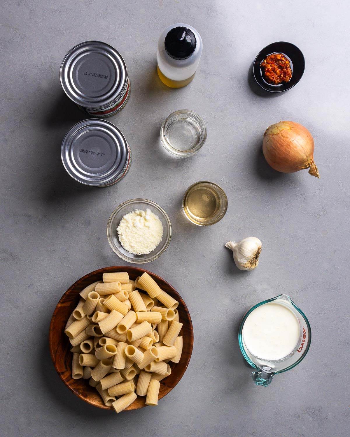 Ingredients shown: 2 cans of plum tomatoes, olive oil, Calabrian chili paste, vodka, wine, onion, pecorino, garlic, rigatoni, and cream.
