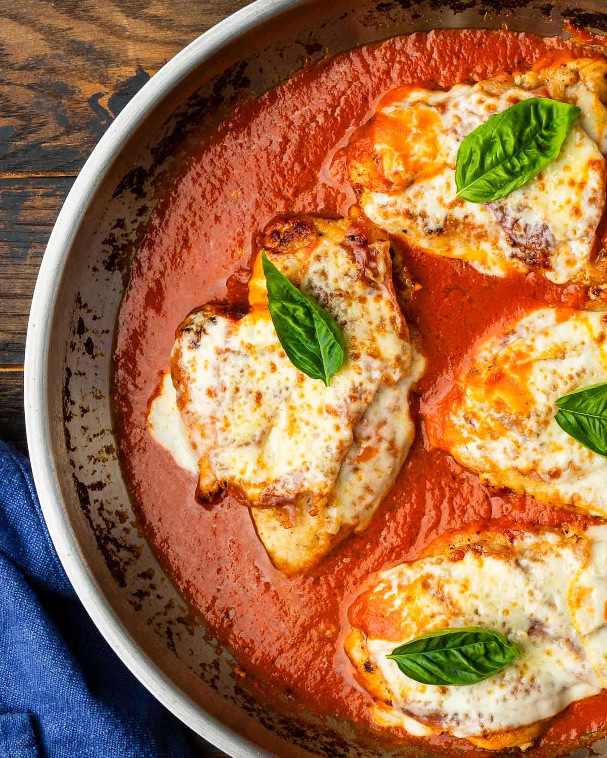 Stainless steel pan with chicken prosciutto and melted cheese in creamy tomato sauce.