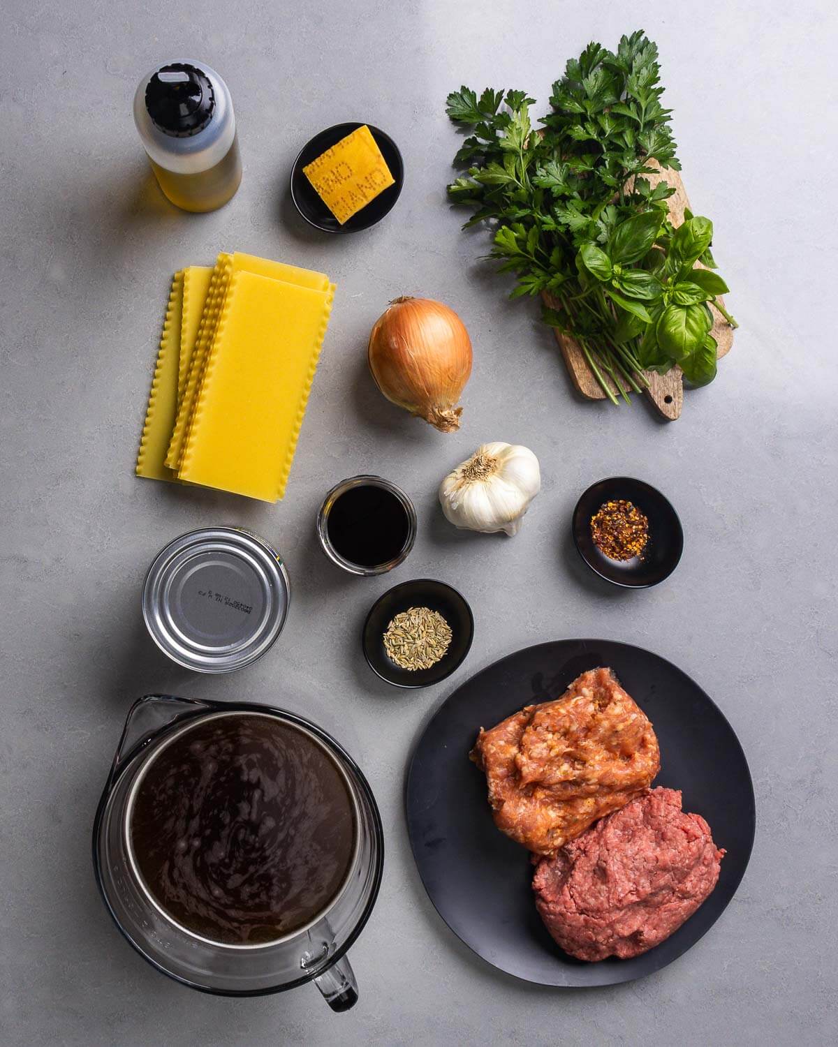 Ingredients shown: olive oil, parmesan rind, parsley, basil, lasagna sheets, onion, garlic, canned tomatoes, red wine, fennel seeds, red pepper flakes, beef stock, ground beef and ground sausage.