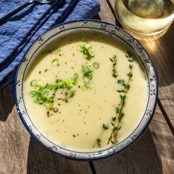 Leek and potato soup in bowl with garnish of thyme and green onions.