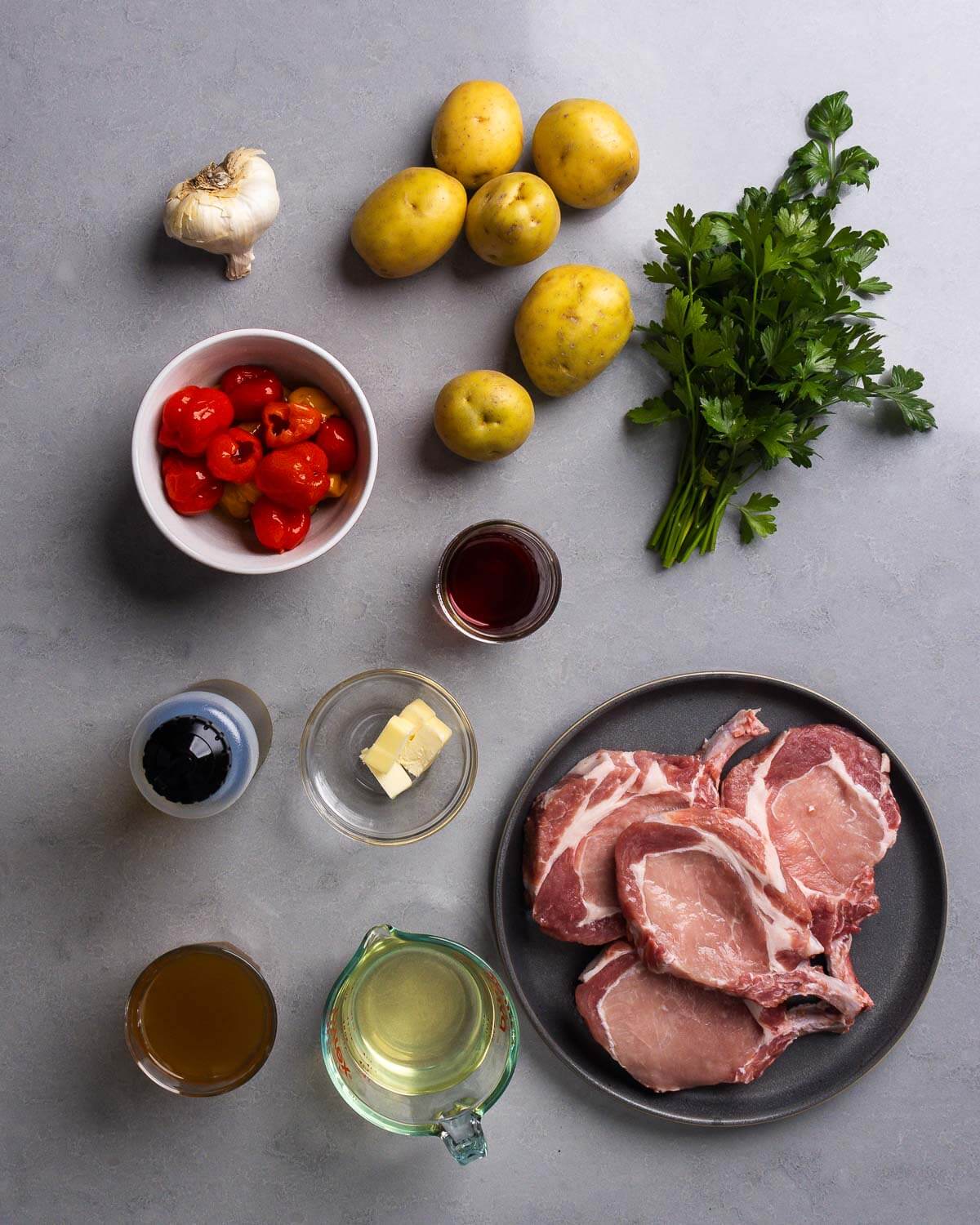 Ingredients shown: garlic, potatoes, parsley, peppadew peppers, red wine vinegar, olive oil, butter, white wine, chicken stock, and pork chops.