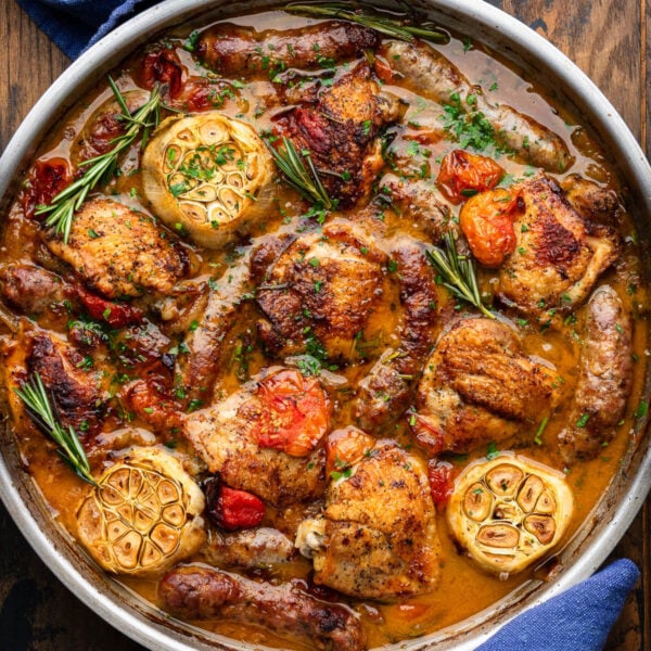 Rosemary chicken with sausage tomatoes and roasted garlic in large pan.