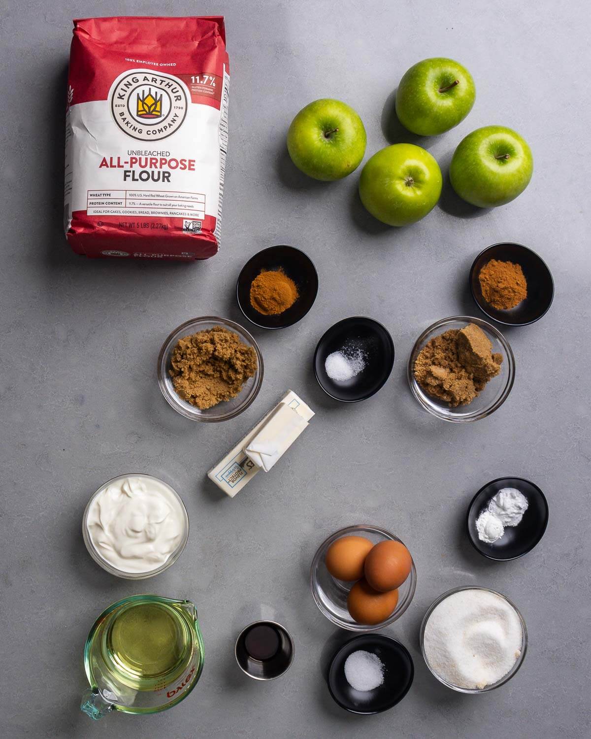 Ingredients shown: flour, apples, cinnamon, brown sugar, salt, butter, sour cream, vegetable oil, vanilla extract, eggs, baking soda, baking powder, and granulated sugar.