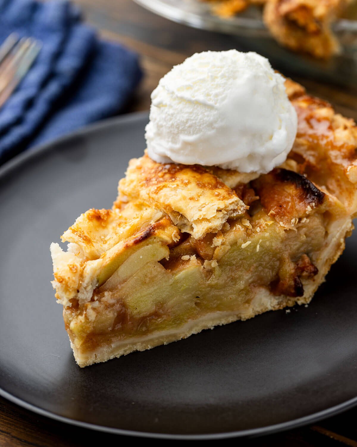 Slice of apple pie with vanilla ice cream in black plate.