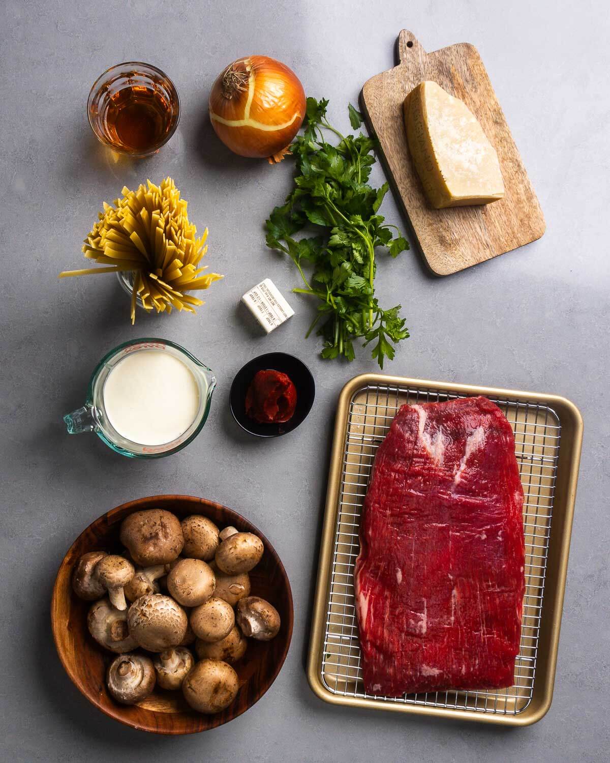 Ingredients shown: bourbon, onion, parlsye, parmesan block, fettuccine, butter, heavy cream, tomato pasta, mushrooms, and flank steak.