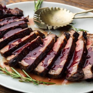 Sliced ribeye steak with red wine sauce on platter.