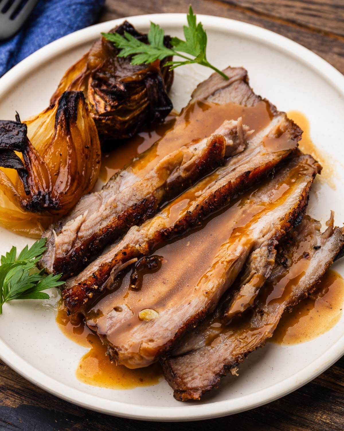 White plate with sliced roasted pork shoulder and gravy.