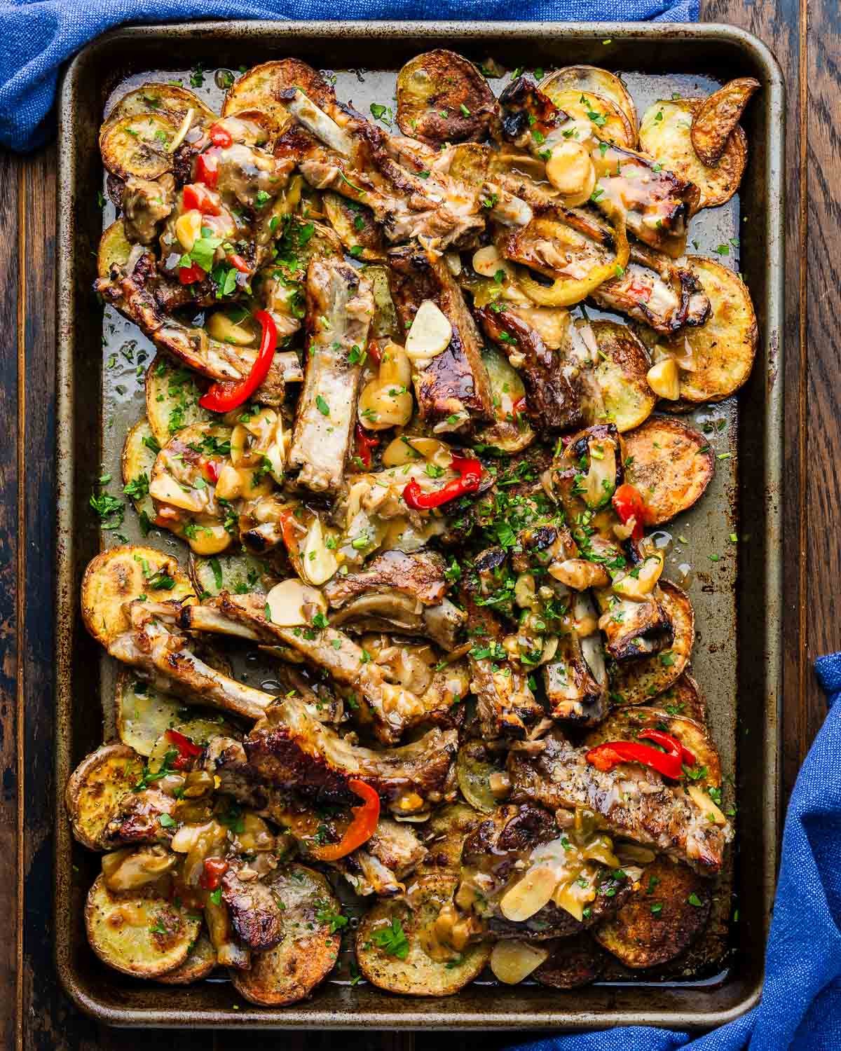 Sticky ribs with crispy potatoes in large sheet pan with blue napkins.