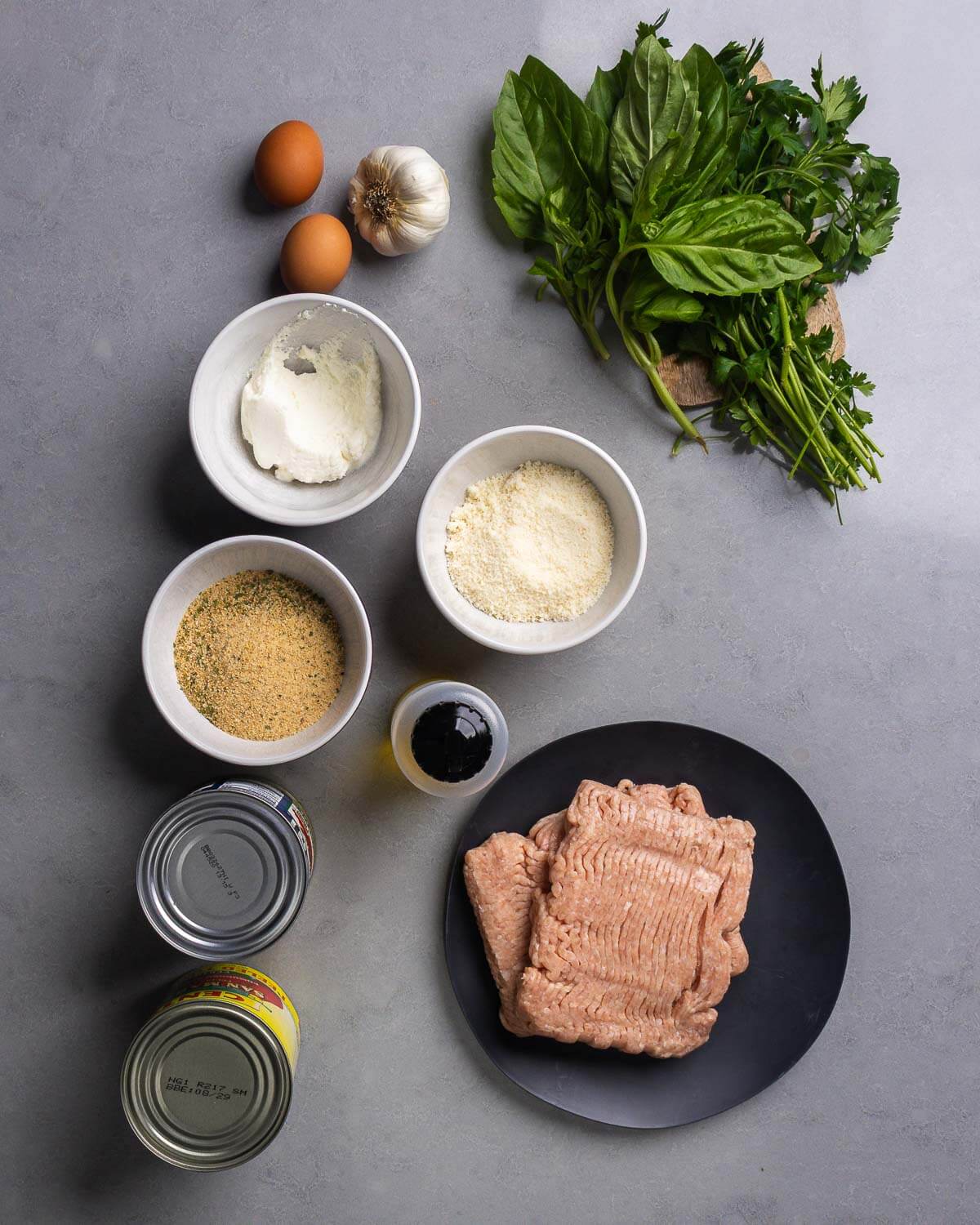 Ingredients shown: eggs, garlic, basil, parsley, ricotta, parmesan cheese, breadcrumbs, olive oil, canned tomatoes, and ground chicken.