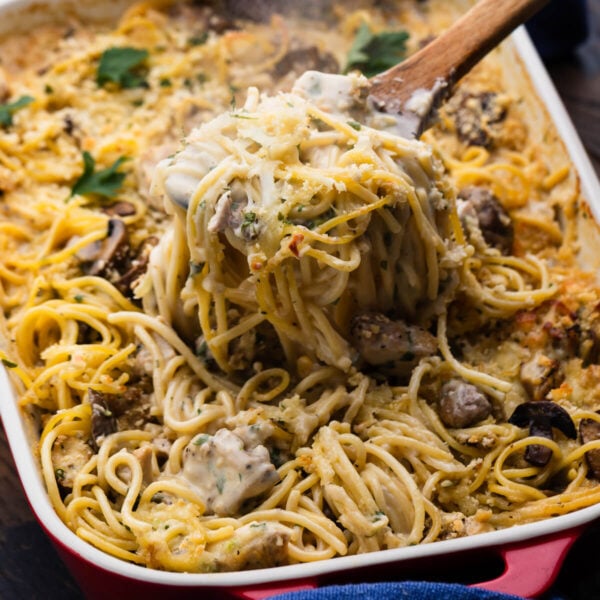 Spoon scooping out a portion of chicken tetrazzini from baking dish.
