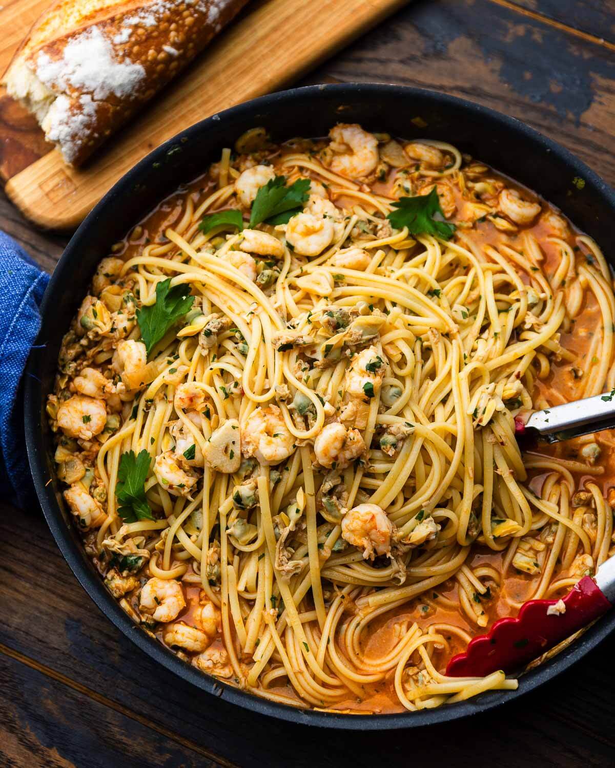 Clam and baby shrimp pasta in pan with loaf of crusty bread.