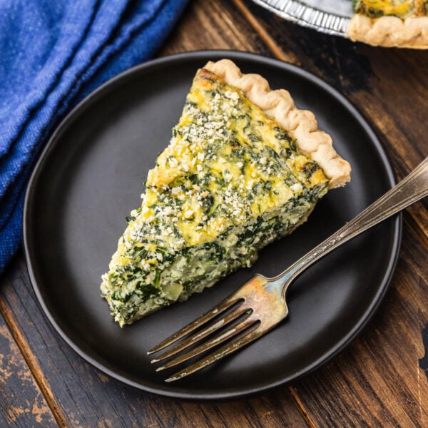 Slice of spinach ricotta pie on black plate.