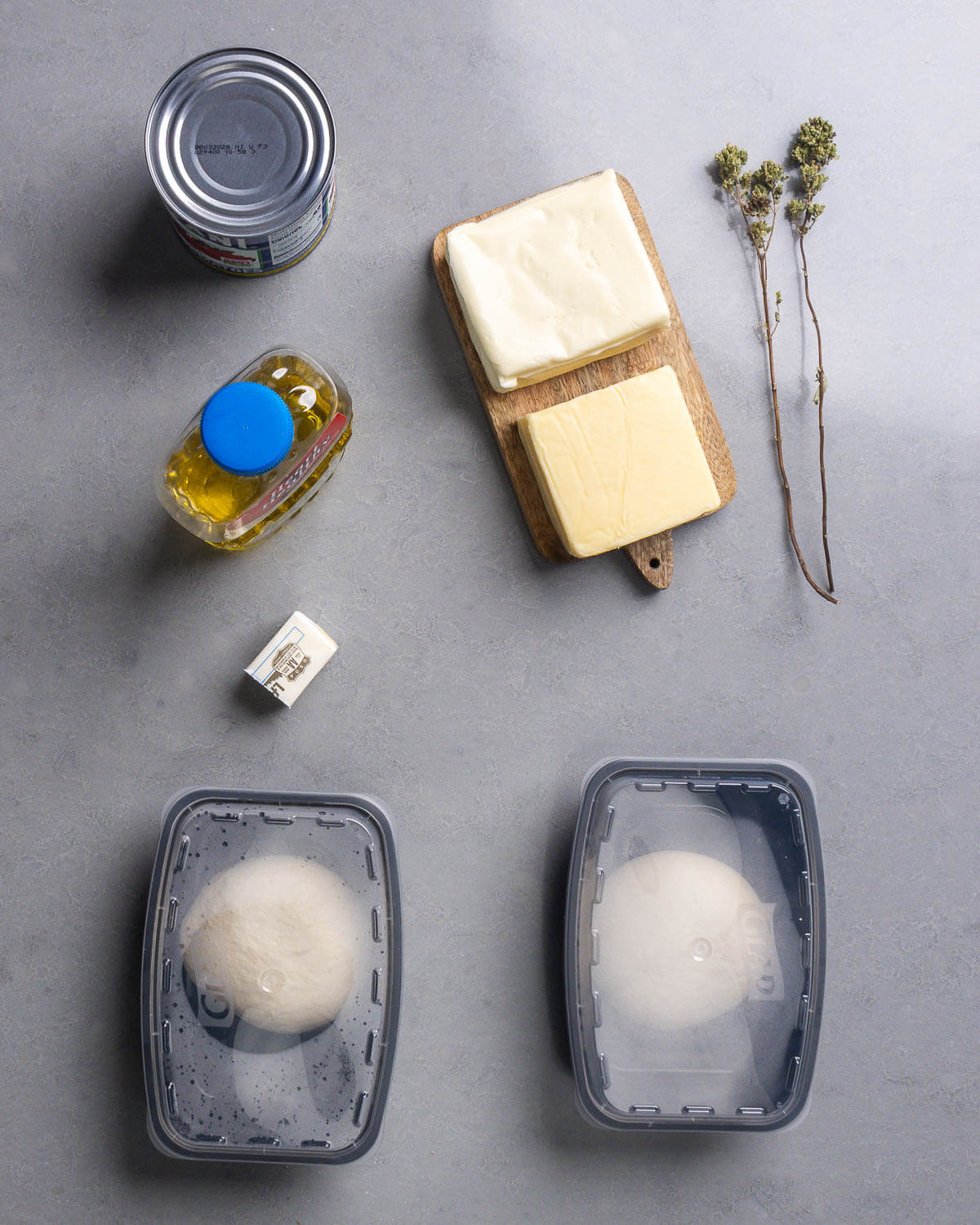 Ingredients shown: can of crushed tomatoes, corn oil, blocks of mozzarella and mild cheddar, Sicilian oregano, butter, and 2 dough balls.