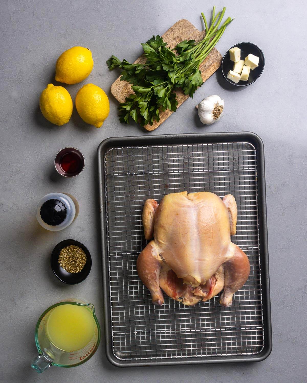Ingredients shown: lemons, parsley, cubed butter, garlic, red wine vinegar, olive oil, oregano, chicken stock, and whole chicken.