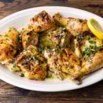 Broiled lemon chicken in platter garnished with parsley and lemon slices.
