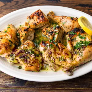 Broiled lemon chicken in platter garnished with parsley and lemon slices.