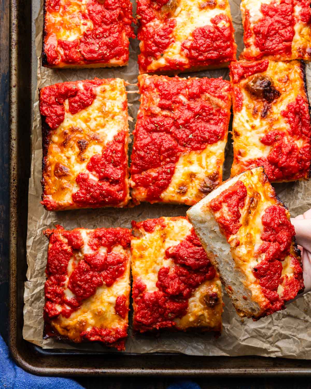 Detroit pizza in pan with one slice held in hands.