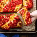 Hands holding slice of Detroit pizza.