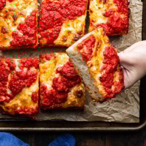 Hands holding slice of Detroit pizza.