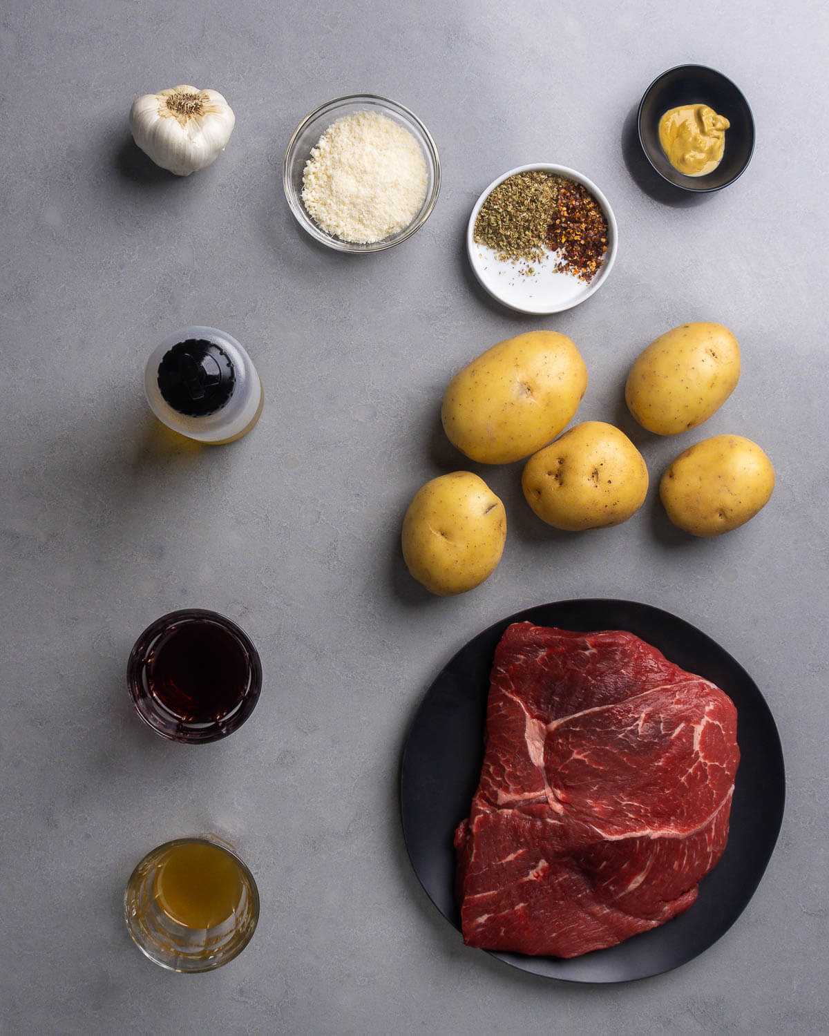 Ingredients shown: garlic, parmesan cheese, dried oregano, hot red pepper flakes, dijon mustard, olive oil, potatoes, red wine vinegar, chicken stock, and sirloin steak.