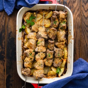 Baking dish with roasted potatoes and parmesan steak skewers.