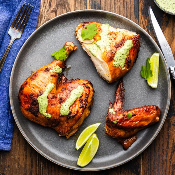 Grey plate with Peruvian chicken pieces topped with green sauce.