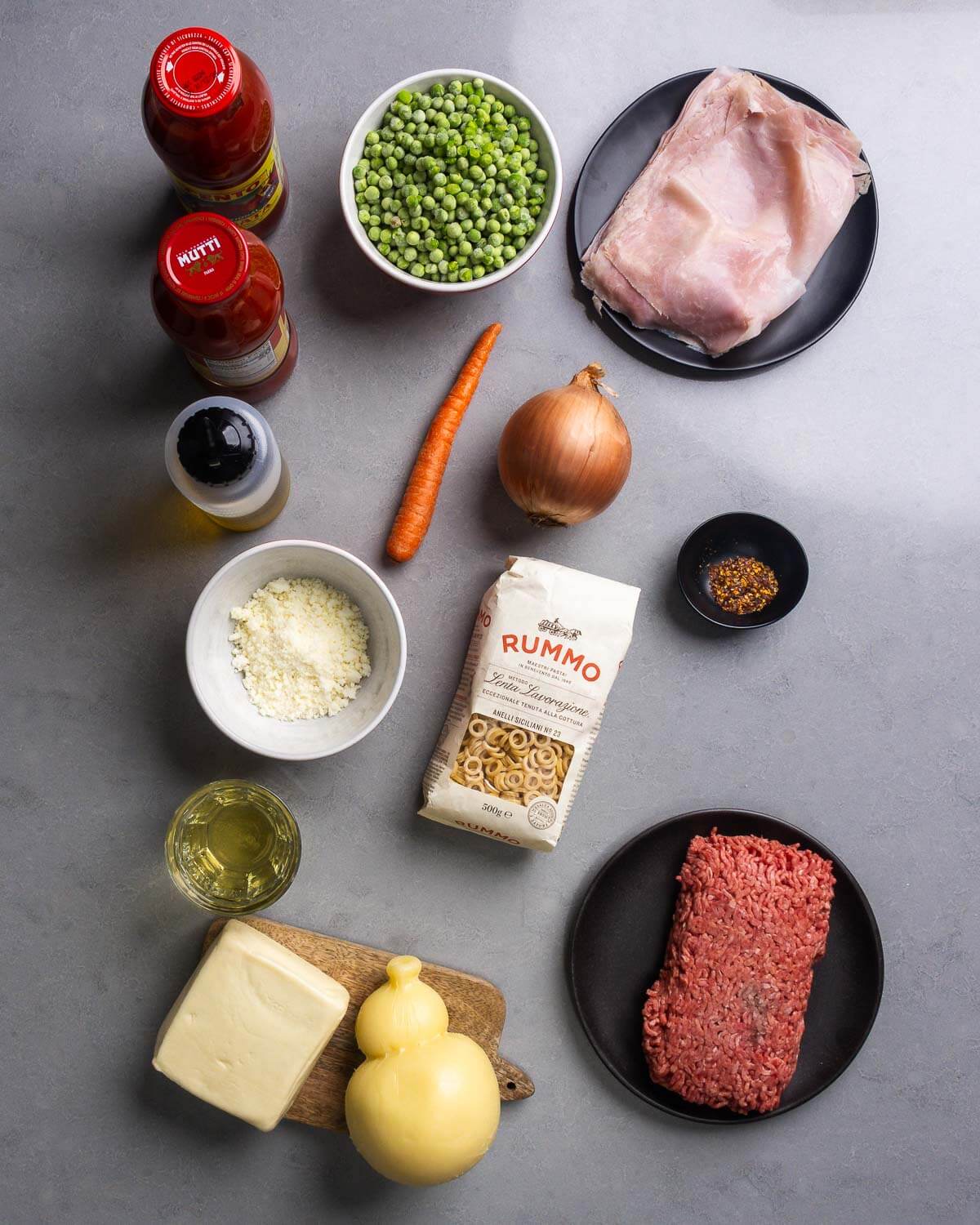 Ingredients shown: 2 jars of passata, olive oil, peas, carrout, ham, onion, pecorino romano, anelletti pasta, hot red pepper flakes, wine, mozzarella, caciocavallo, and ground beef.