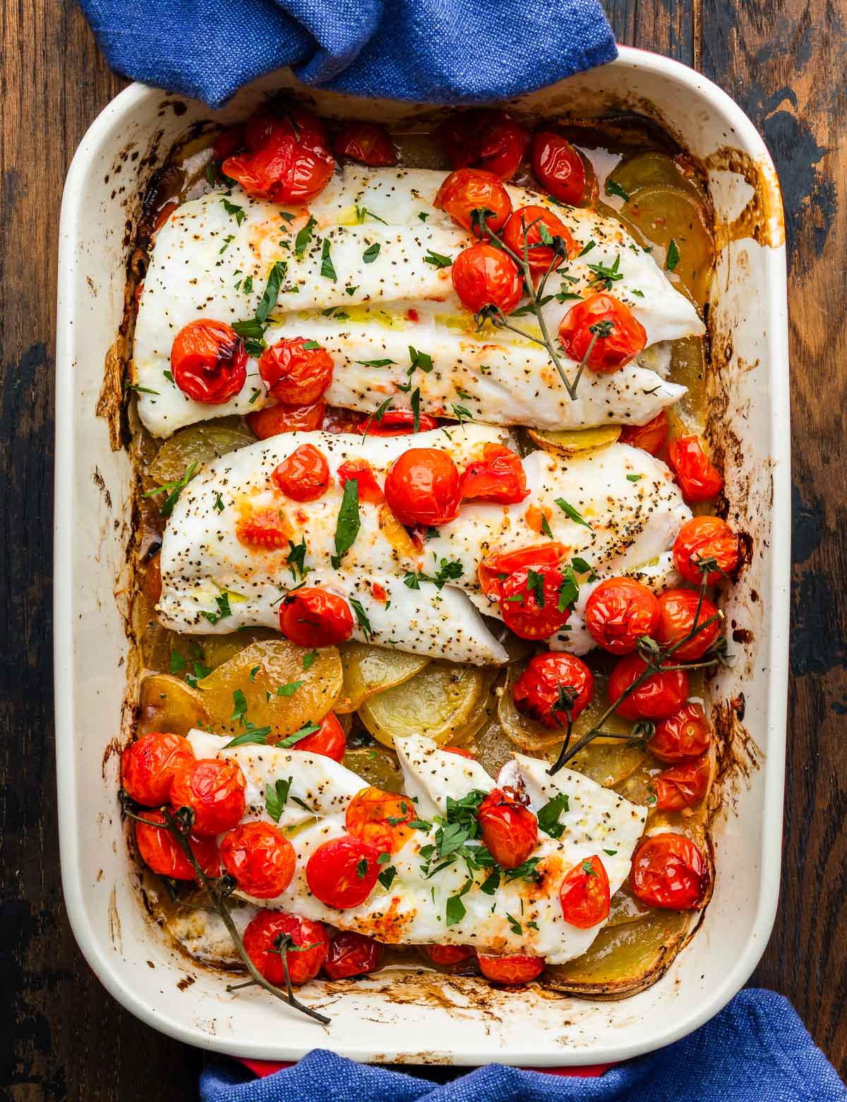 Large baking dish with baked cod, lemon potatoes, and cherry tomatoes.