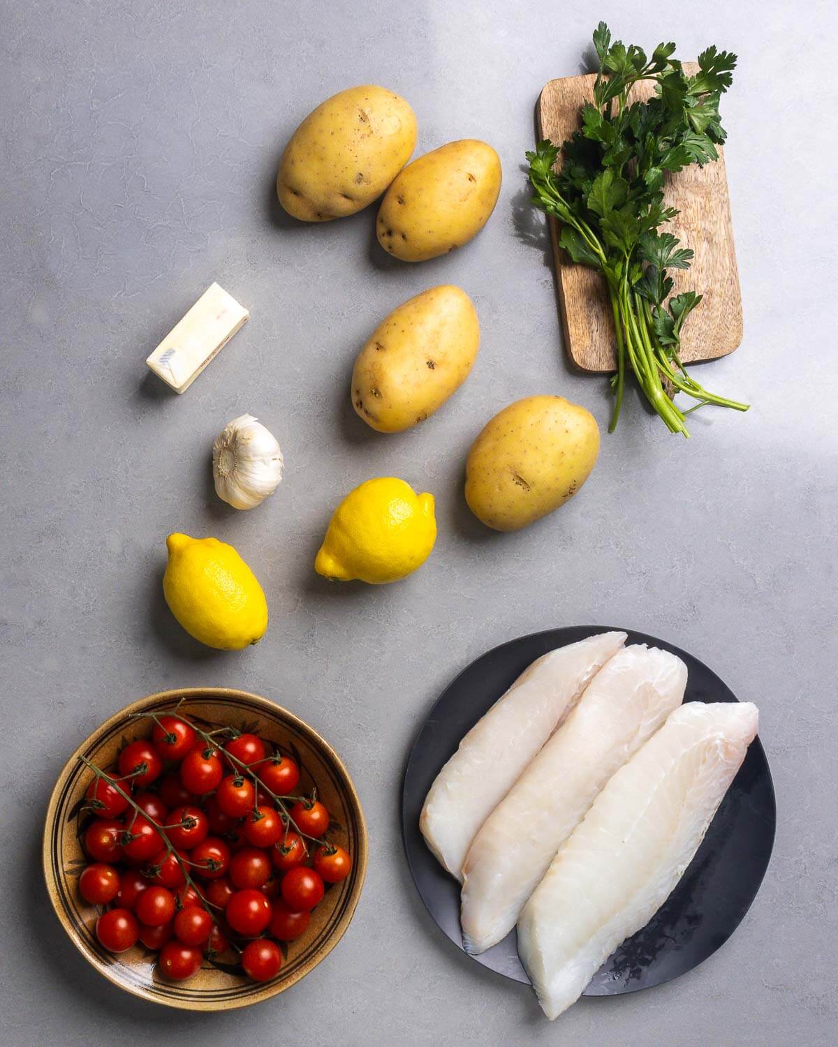 Ingredients shown: butter, potatoes, parsley, lemons, cherry tomatoes, and cod fillets.