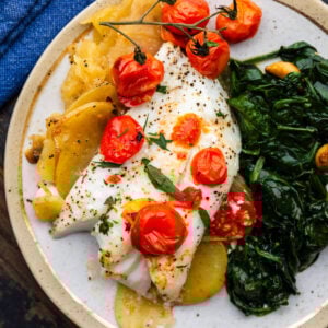 Baked cod with lemon potatoes and cherry tomatoes on white plate.