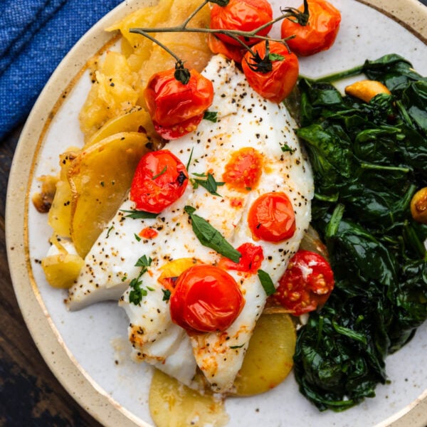 Baked cod with lemon potatoes and cherry tomatoes on white plate.