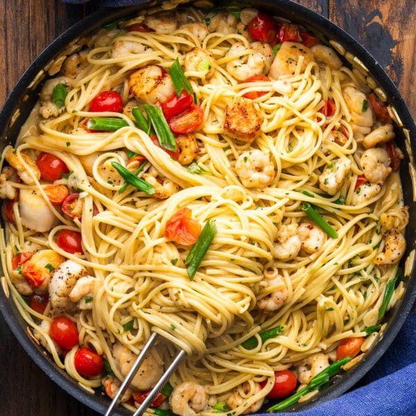 Large black with creamy seafood pasta and kitchen tweezers.