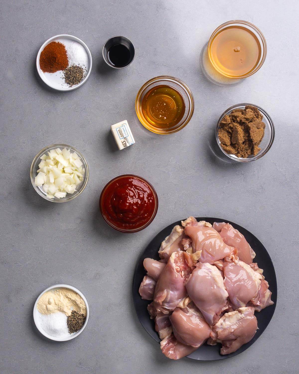 Ingredients shown: spices, worcestershire sauce, butter, honey, apple cider vinegar, dark brown sugar, onion, ketchup, and boneless skinless chicken thighs.