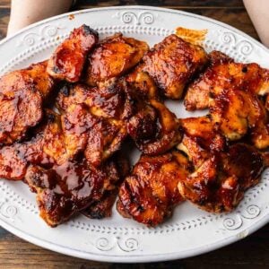 Hands holding platter of barbecue chicken thighs.