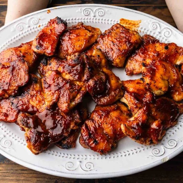 Hands holding platter of barbecue chicken thighs.