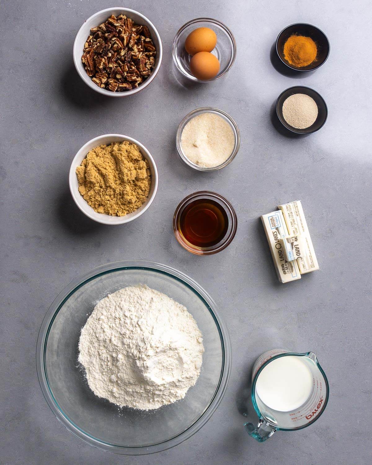 Ingredients shown: chopped pecans, eggs, cinnamon, yeast, sugar, brown sugar, corn syrup, butter, flour, and milk.