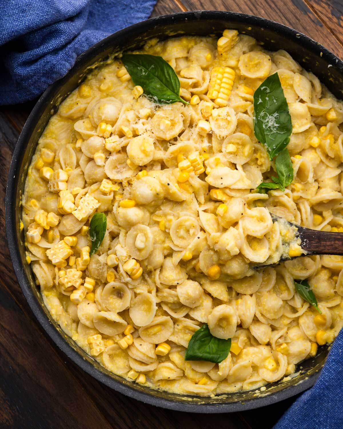 Black pan with creamy corn pasta topped with basil leaves.