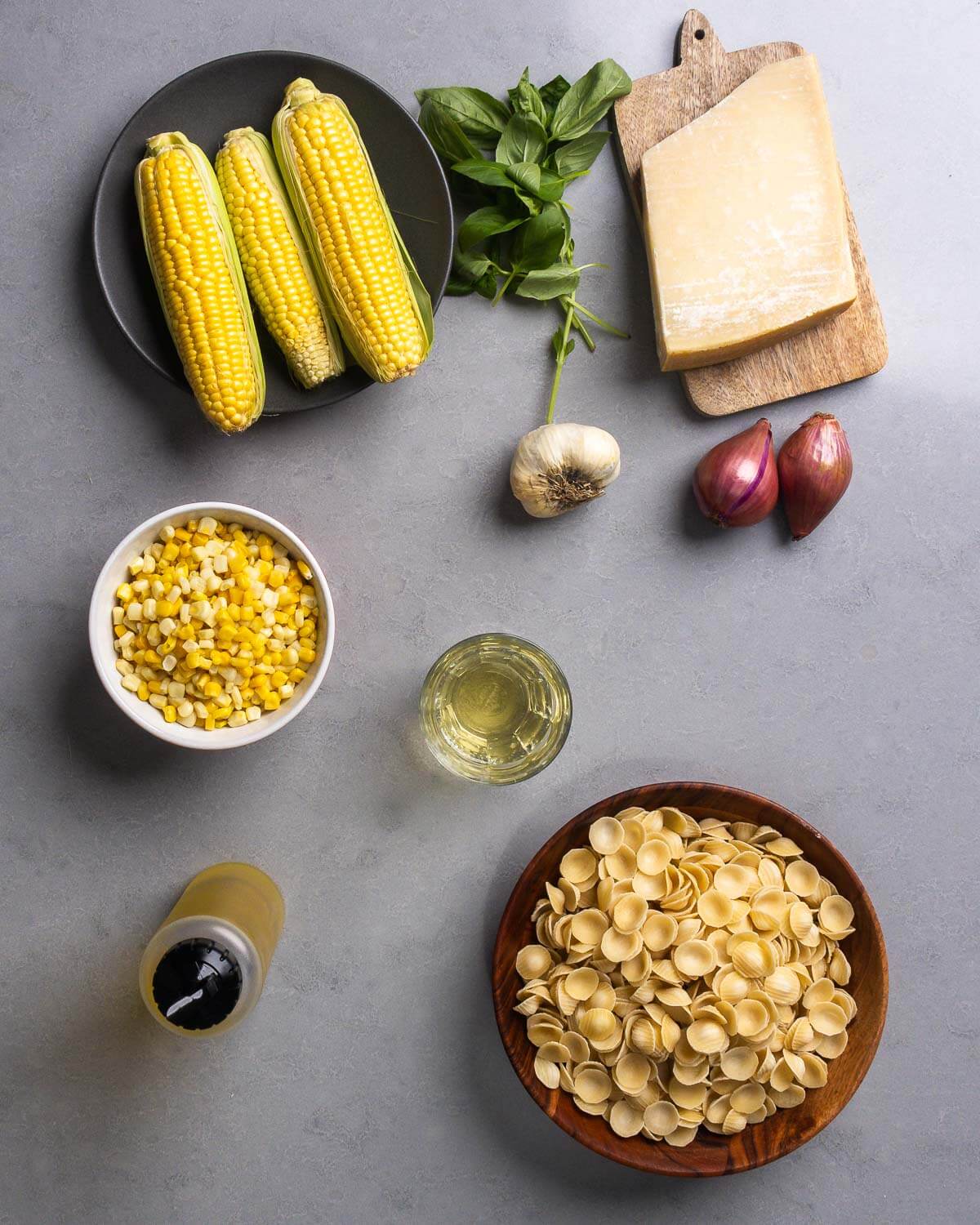 Ingredients shown: corn cobs and frozen kernels, basil, parmigiano reggiano, garlic, shallots, white wine, olive oil, and orecchiette pasta.