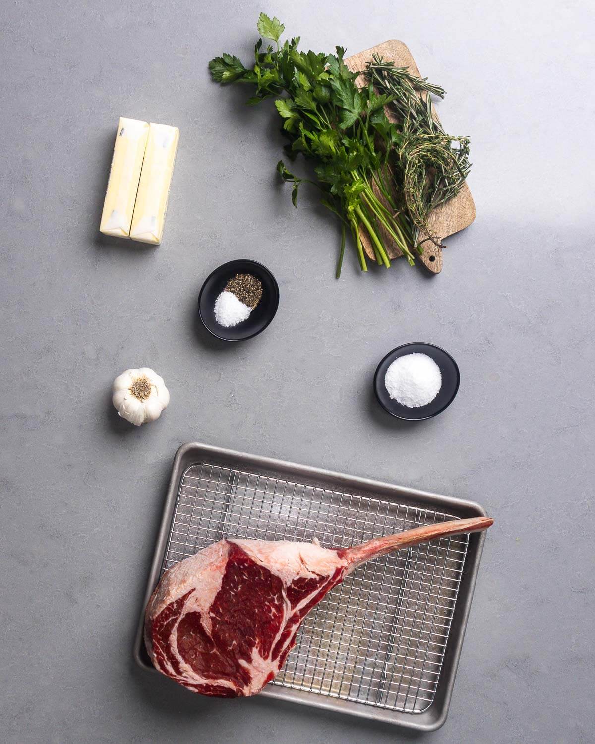 Ingredients shown: butter, parsley, thyme, rosemary, salt, pepper, garlic, and large tomahawk steak.