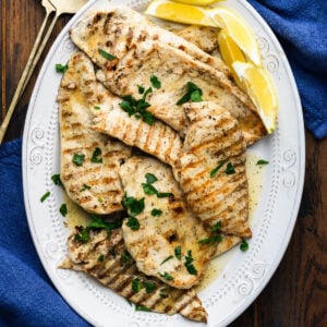 Platter of marinated grilled chicken topped with parsley and served with lemon wedges.