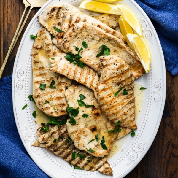 Platter of marinated grilled chicken topped with parsley and served with lemon wedges.