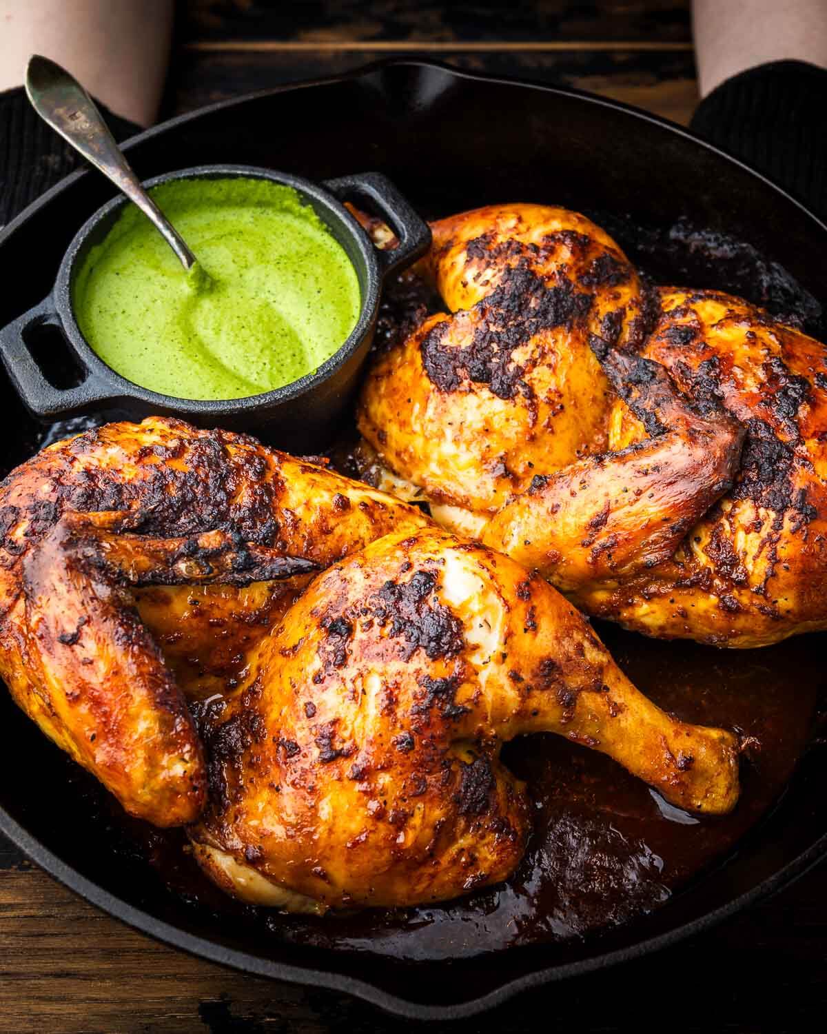 Peruvian chicken in cast iron pan with side of green sauce.