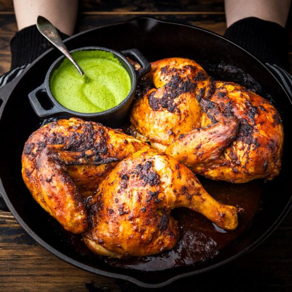 Hands holding pan with Peruvian chicken with side of green sauce.